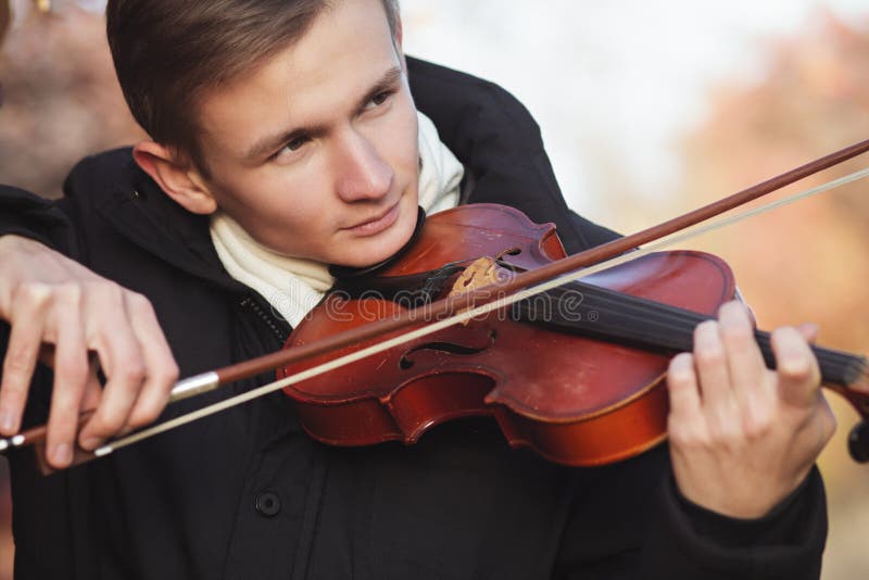 Face profile of a young elegant man playing the violin on autumn nature backgroung, a boy with a bowed orchestra instrument makes a concert, concept of classical music, hobby and art