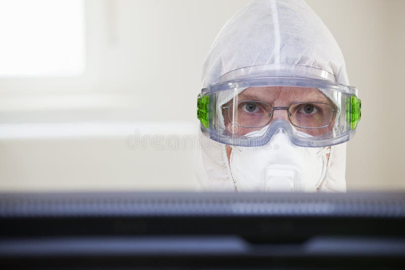 Face of a tired doctor with protective clothing an medical mask behind a computer monitor in a hospital stock photos Face of a tired doctor with protective clothing an medical mask behind a computer monitor in a hospital stock photos