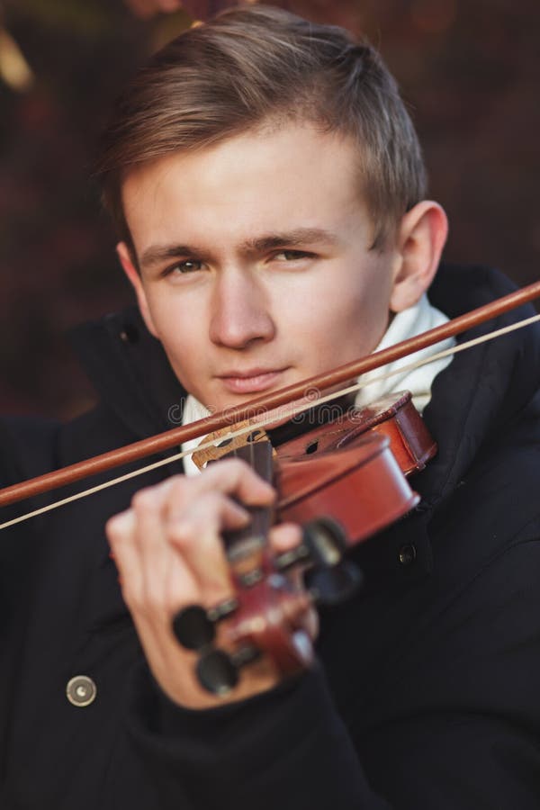 Face of a young elegant man playing the violin on autumn nature backgroung, a boy with a bowed instrument practicing, musical performance outdoors, concept of hobby and art