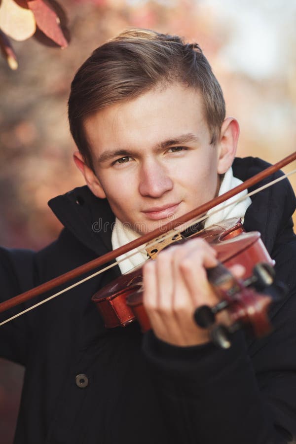 Face of a young elegant man playing the violin on autumn nature backgroung, a boy with a bowed instrument practicing, musical performance outdoors, concept of hobby and art