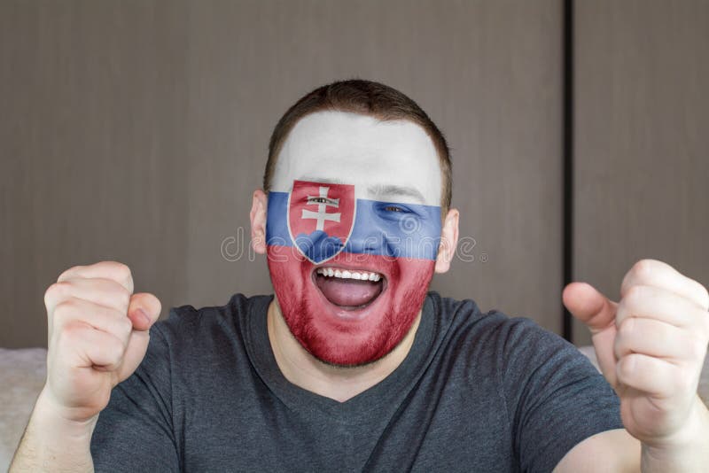 Tvár mladého kričiaceho muža pomaľovaného vlajkou Slovenska. Fanúšik futbalového tímu.
