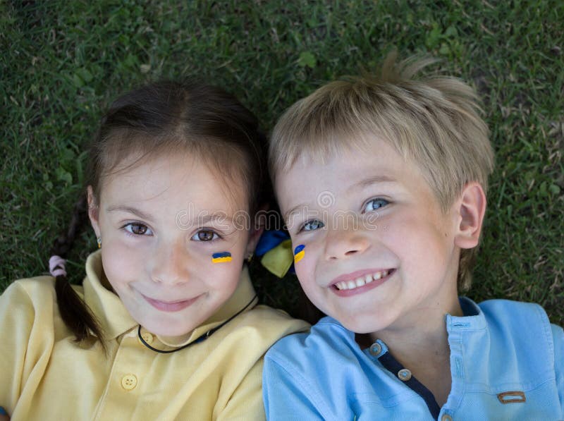 Faces of a happy boy and girl 6-7 years old in yellow and blue T-shirts smile joyfully, lying on the grass