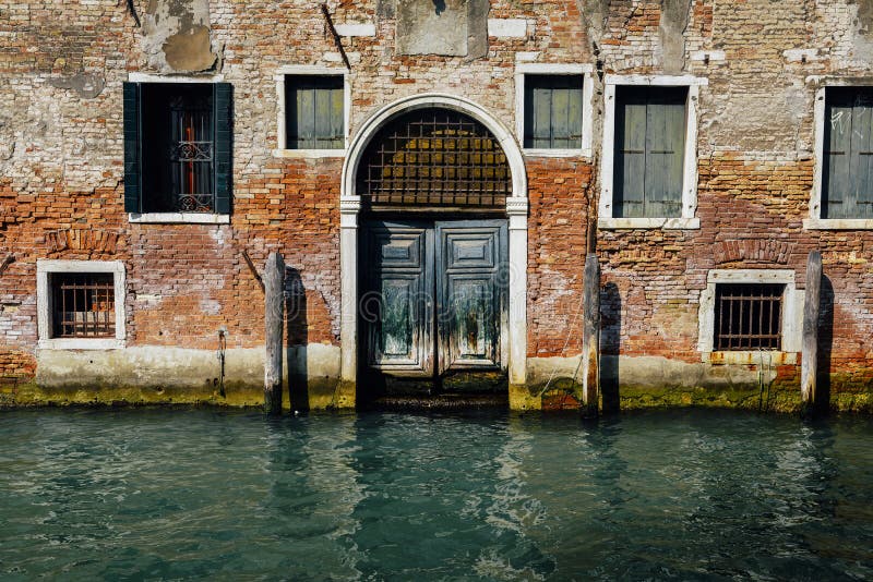 Fachada da casa velha parcialmente musgoso do tijolo com a porta de madeira do vintage no canal estreito em Veneza, Itália fotografia de stock royalty free Fachada da casa velha parcialmente musgoso do tijolo com a porta de madeira do vintage no canal estreito em Veneza, Itália fotografia de stock royalty free