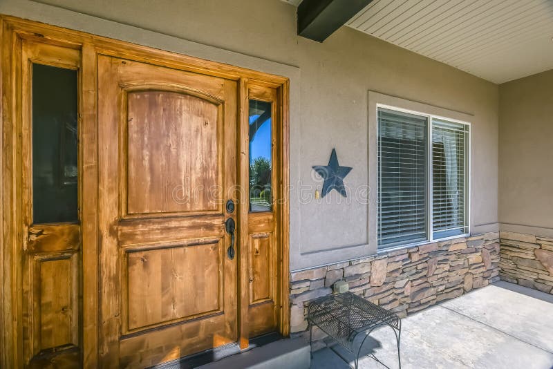 Fachada del hogar con la puerta de madera y el pórtico iluminado por el sol imagenes de archivo Fachada del hogar con la puerta de madera y el pórtico iluminado por el sol imagenes de archivo