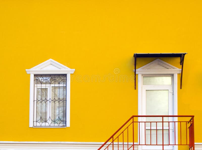Fachada do edifício em que existe uma porta branca de entrada e uma janela branca. a parede da casa é amarelo brilhante. a fotografia de stock royalty free