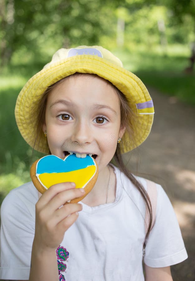 facial portrait of joyful girl 7 years old with a gingerbread painted in the yellow-blue colors of the Ukrainian flag