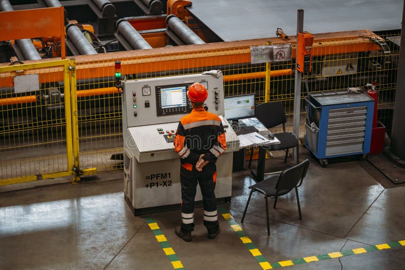 Factory worker monitoring CNC machine in metalworking workshop.