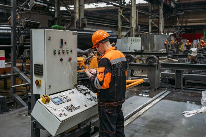 Factory worker monitoring CNC machine in metalworking workshop.