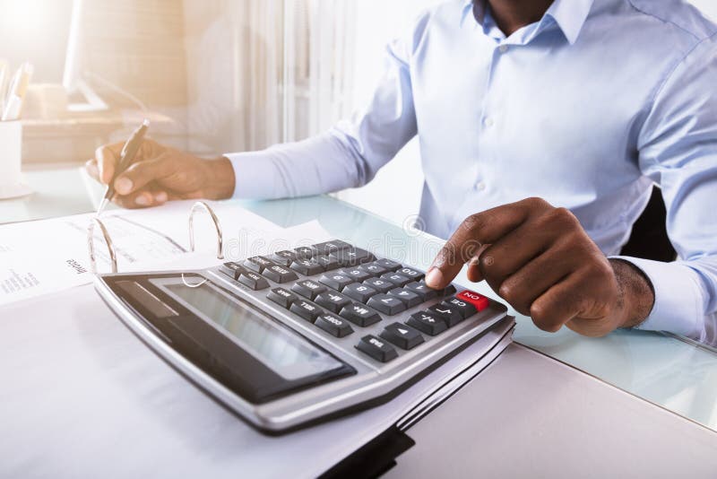 Close-up Of A Businessman Calculating Invoice Using Calculator At Workplace. Close-up Of A Businessman Calculating Invoice Using Calculator At Workplace