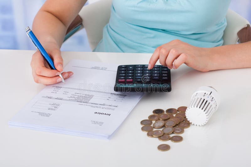 Midsection of young woman calculating invoice by coins and thermostat at desk. Midsection of young woman calculating invoice by coins and thermostat at desk