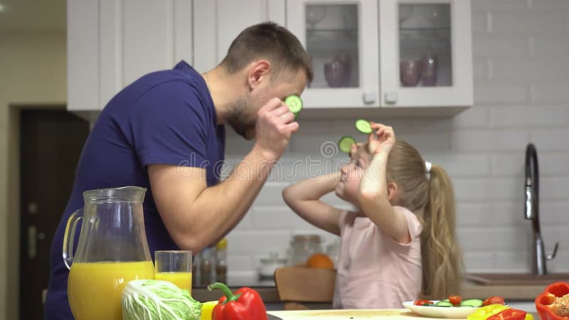 Fader och dotter har kul med att laga mat i köket medan de leker med grönsaker arkivfilmer