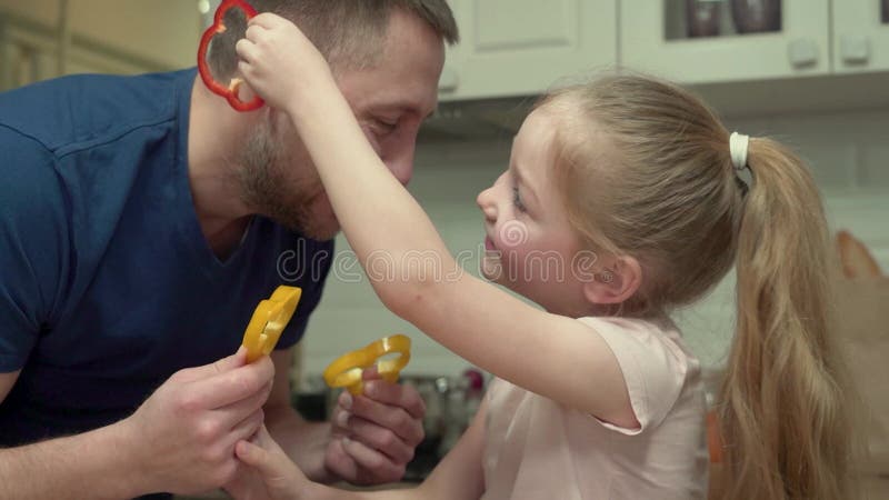 Fader och dotter leker tillsammans med grönsaker i köket stock video