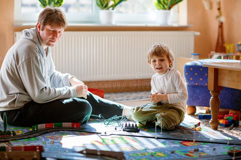 Fader och son leker med racerbilar på racerbangårdar inomhus med bilar. Glad liten förskolepojke och ung man arkivfoto