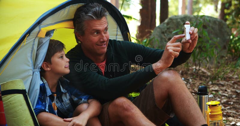 Fader och son som tar en selfie på mobiltelefonen utanför tältet