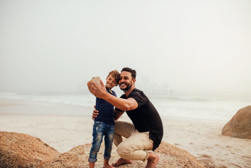 Fader och son som tar selfie på den steniga stranden arkivbilder Fader och son som tar selfie på den steniga stranden arkivbilder