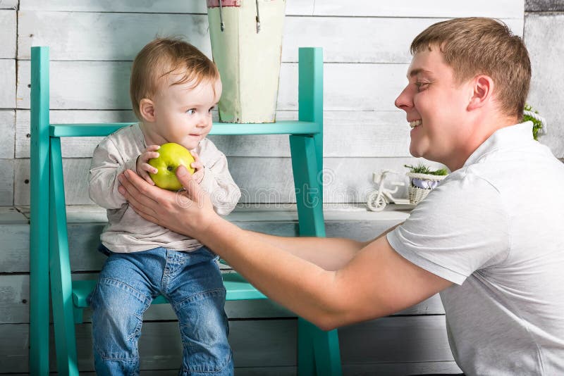 Fadern ger sig för att behandla som ett barn det stora gröna äpplet för pojken Han båda är i jeans och den vita hoodien Farsan me royaltyfria foton Fadern ger sig för att behandla som ett barn det stora gröna äpplet för pojken Han båda är i jeans och den vita hoodien Farsan me royaltyfria foton