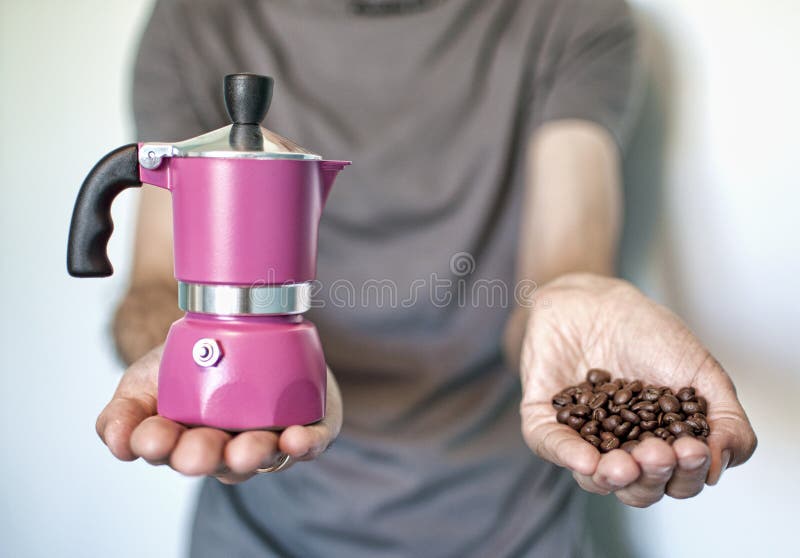 Fagioli dentellare del creatore e del coffe di caffè. Giovane che tiene un creatore di caffè dentellare in una mano e nell'altra un la manciata di chicchi di caffè