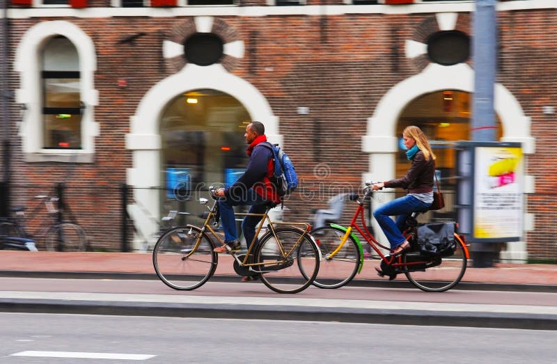 Amsterdam, 2010 - Blur effect from Focus Continuous mode. Young woman riding a colorful bike and man overtaking her on a golden bicycle. Amsterdam, 2010 - Blur effect from Focus Continuous mode. Young woman riding a colorful bike and man overtaking her on a golden bicycle.