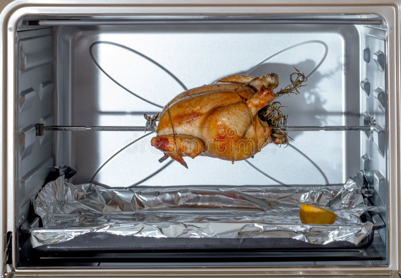 Fresh chicken, trussed, stuffed with herbs and cooking on a spit in a domestic oven. Fresh chicken, trussed, stuffed with herbs and cooking on a spit in a domestic oven