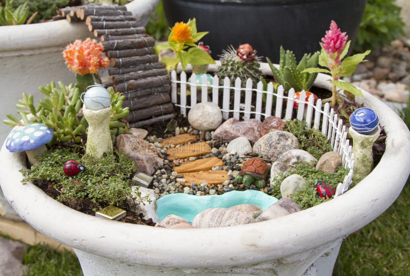 Fairy garden in a flower pot outdoors. Fairy garden with a white picket fence, gazing balls and pond in a flower pot stock photos