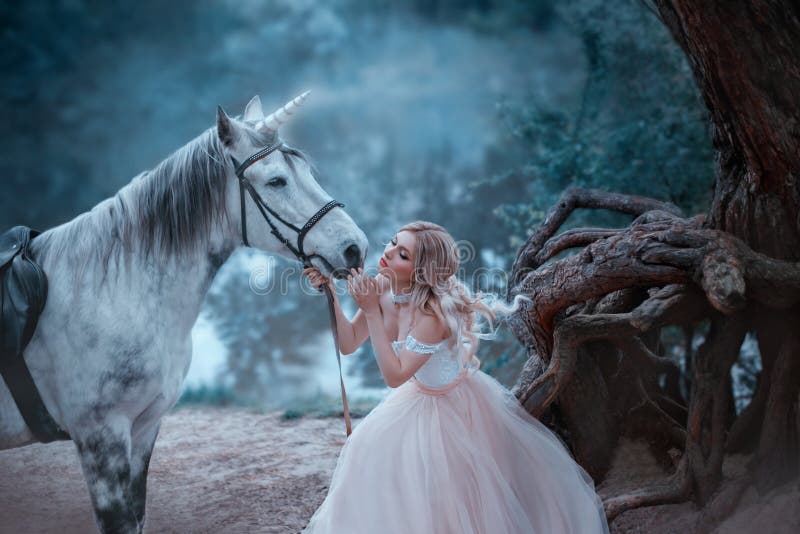 A fairy in a tender vintage dress hugs a unicorn. Fantastic magical, radiant horse. Background river and forest. Blonde girl with wavy hair - light elf. Artistic Photography
