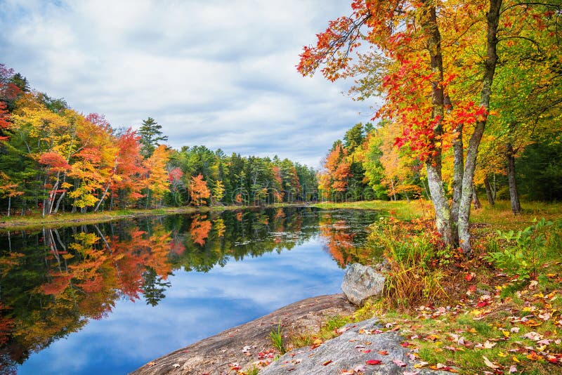 Fall foliage colors reflected in still lake water in New England