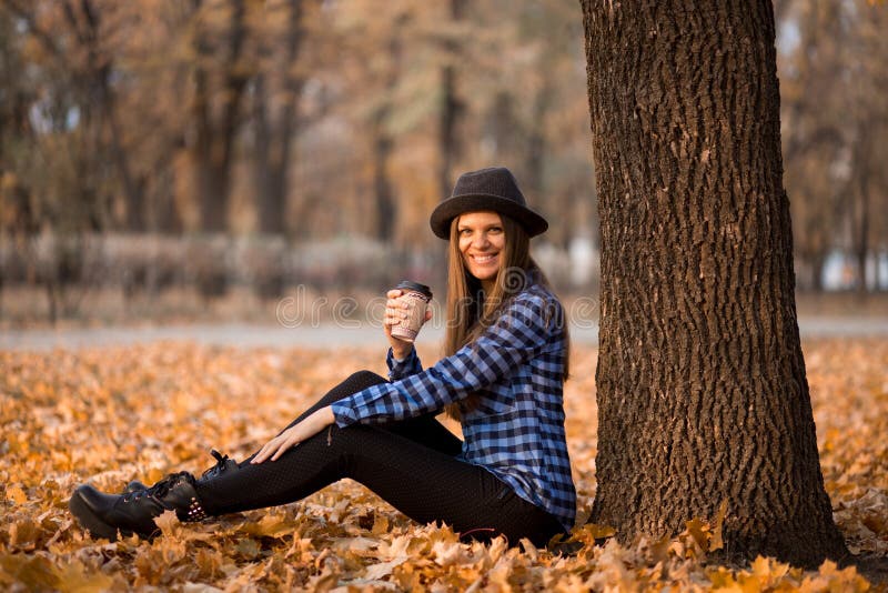 Fall-Konzept _glücklich und nett Frau in Hut, trinken Kaffee während sitzen auf Park Blatt lizenzfreie stockfotografie Fall-Konzept _glücklich und nett Frau in Hut, trinken Kaffee während sitzen auf Park Blatt lizenzfreie stockfotografie