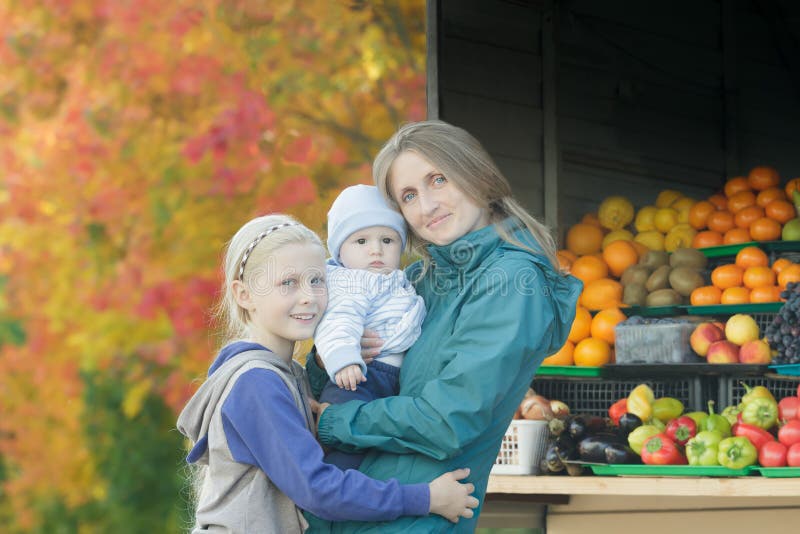 Fall street outdoor family portrait of mother and two siblings at bright fall tree leaves and fruit stand background royalty free stock photography Fall street outdoor family portrait of mother and two siblings at bright fall tree leaves and fruit stand background royalty free stock photography