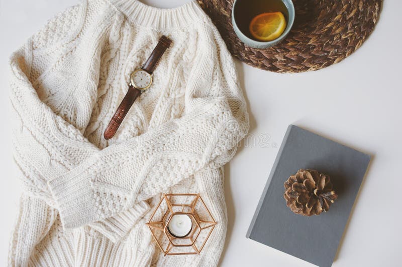 Fall or winter cozy still life set. Warm knitted sweater, cup of tea with lemon, and book with pine cone on white background