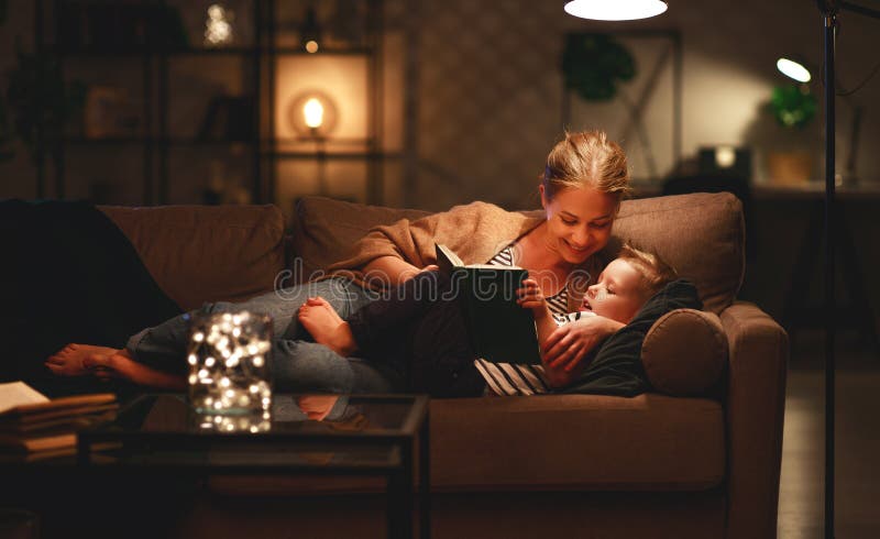 A fam?lia antes da m?e indo para a cama l? a seu livro do filho da crian?a perto de uma l?mpada na noite foto de stock royalty free A fam?lia antes da m?e indo para a cama l? a seu livro do filho da crian?a perto de uma l?mpada na noite foto de stock royalty free