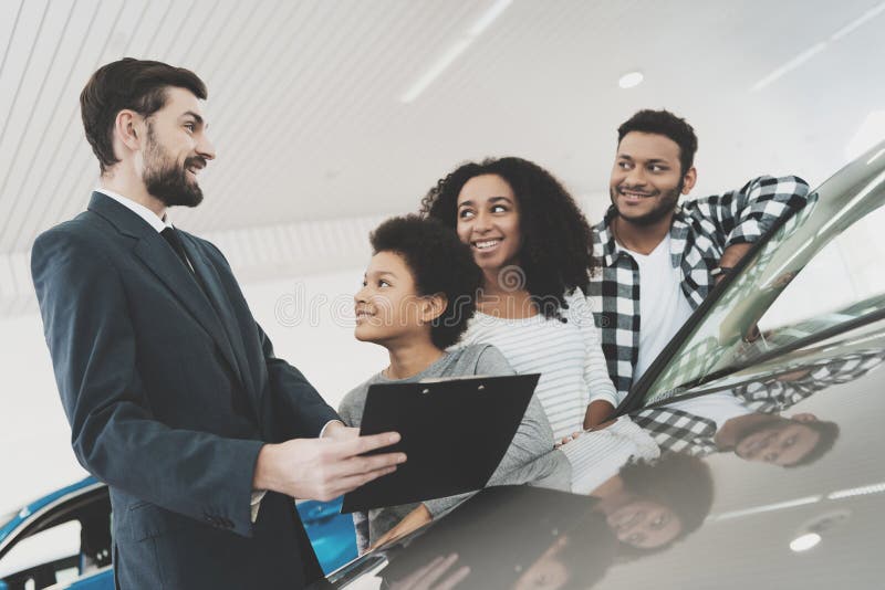 Famiglia afroamericana al concessionario auto Il rappresentante sta dando le carte per la nuova automobile immagine stock libera da diritti