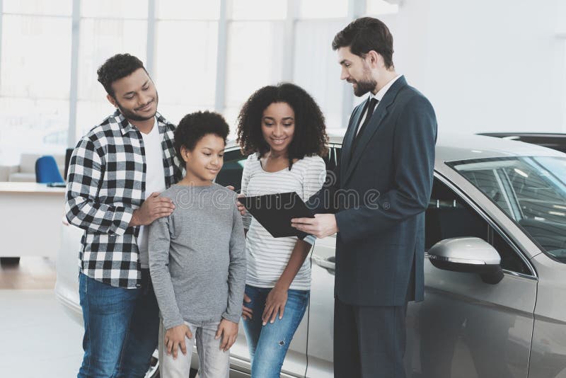 Famiglia afroamericana al concessionario auto Il rappresentante sta firmando le carte per la nuova automobile immagini stock