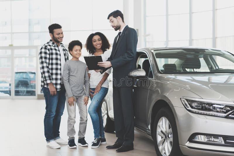 Famiglia afroamericana al concessionario auto Il rappresentante sta firmando le carte per la nuova automobile immagini stock