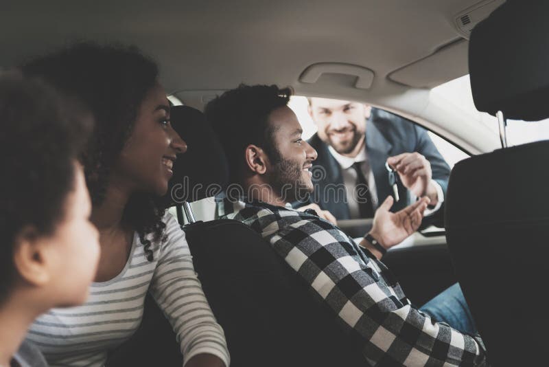 Famiglia afroamericana al concessionario auto Il rappresentante sta fornendo le chiavi per la nuova automobile immagini stock libere da diritti
