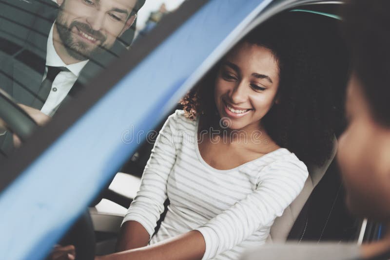 Famiglia afroamericana al concessionario auto Il rappresentante sta mostrando la nuova automobile fotografie stock libere da diritti
