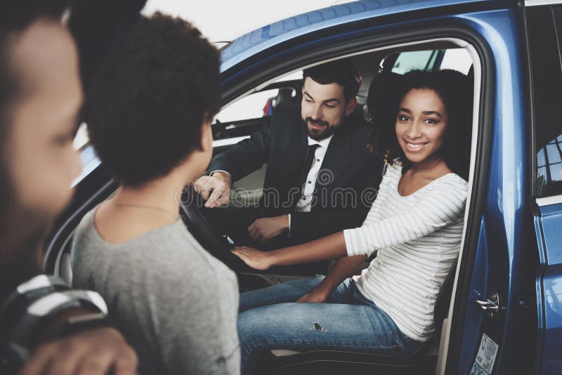 Famiglia afroamericana al concessionario auto Il rappresentante sta mostrando la nuova automobile fotografia stock libera da diritti