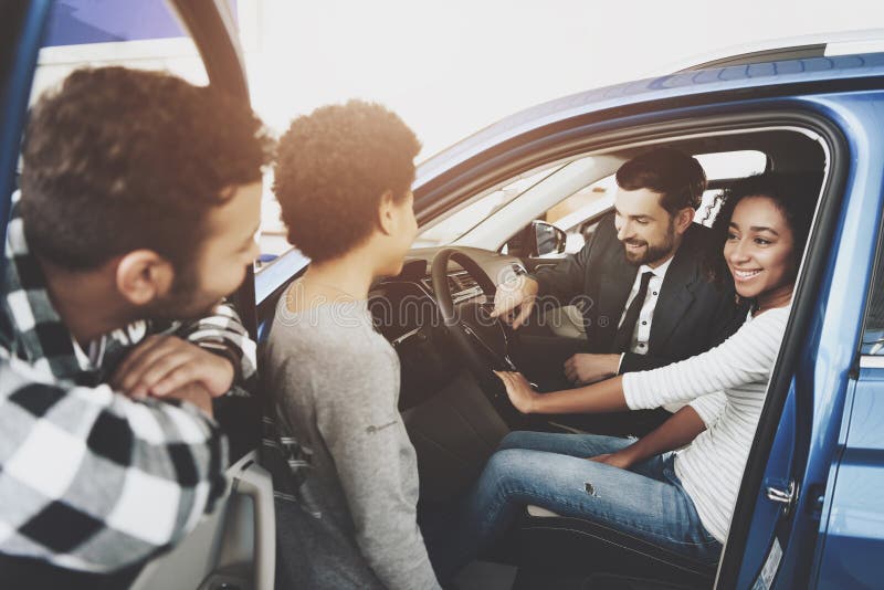 Famiglia afroamericana al concessionario auto Il rappresentante sta mostrando la nuova automobile fotografia stock libera da diritti