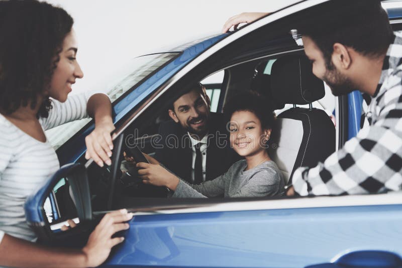 Famiglia afroamericana al concessionario auto Il rappresentante sta mostrando la nuova automobile al ragazzo immagine stock