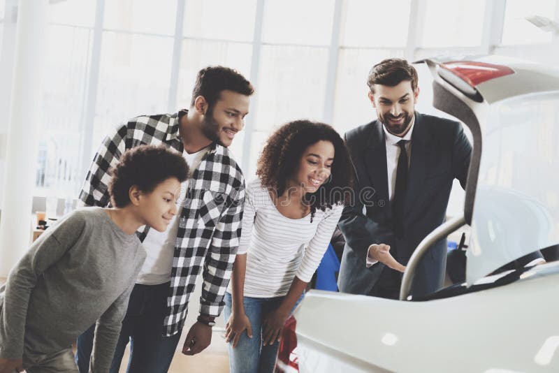 Famiglia afroamericana al concessionario auto Il rappresentante sta mostrando il tronco di nuova automobile immagine stock