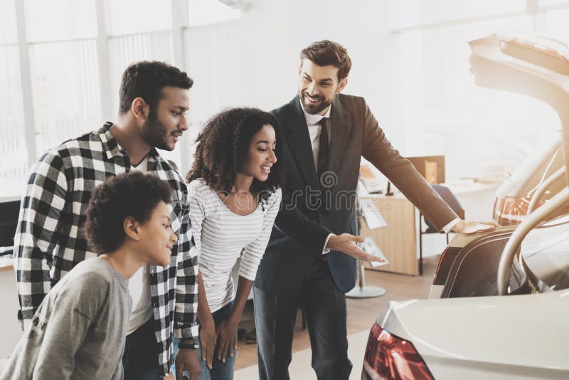 Famiglia afroamericana al concessionario auto Il rappresentante sta mostrando il tronco di nuova automobile immagine stock libera da diritti