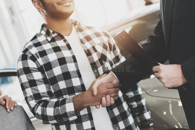 Famiglia afroamericana al concessionario auto Rappresentante ed uomo che stringono le mani, congratulantesi con la nuova automobi immagine stock