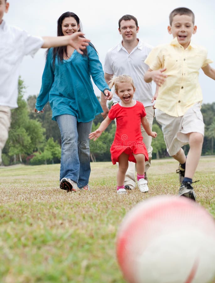 Famiglia allegra che gioca gioco del calcio sul prato inglese verde immagini stock Famiglia allegra che gioca gioco del calcio sul prato inglese verde immagini stock