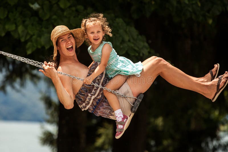 Famiglia amorosa felice! Giovane madre e sua la figlia del bambino che oscillano sulle oscillazioni e che ridono una sera di esta immagine stock libera da diritti Famiglia amorosa felice! Giovane madre e sua la figlia del bambino che oscillano sulle oscillazioni e che ridono una sera di esta immagine stock libera da diritti