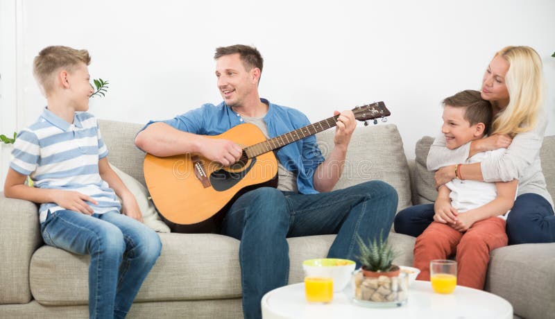 Famiglia caucasica felice che sorride insieme, giocante chitarra e cantante le canzoni a casa moderna accogliente fotografie stock libere da diritti Famiglia caucasica felice che sorride insieme, giocante chitarra e cantante le canzoni a casa moderna accogliente fotografie stock libere da diritti