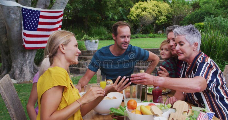 Famiglia caucasica sorridente che fa festa in giardino guardando lo smartphone insieme