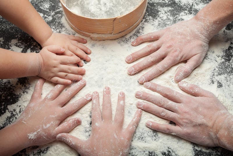 Famiglia che cucina i dolci casalinghi, le mani della mamma e due figlie in farina su un fondo nero della tavola immagine stock Famiglia che cucina i dolci casalinghi, le mani della mamma e due figlie in farina su un fondo nero della tavola immagine stock
