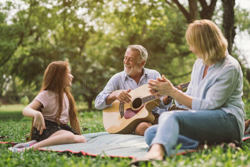 Famiglia che gode del tempo di qualità, giocante chitarra nel loro giardino verde del parco fotografia stock libera da diritti Famiglia che gode del tempo di qualità, giocante chitarra nel loro giardino verde del parco fotografia stock libera da diritti