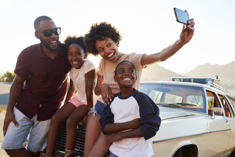 Famiglia che posa per Selfie accanto all'automobile imballata per il viaggio stradale