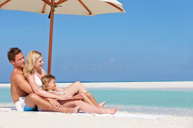 Famiglia che si siede sotto l'ombrello sulla festa della spiaggia immagini stock Famiglia che si siede sotto l'ombrello sulla festa della spiaggia immagini stock