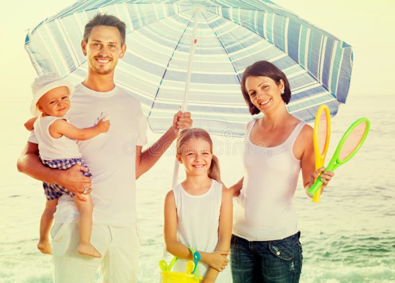 Famiglia che sta sotto l'ombrello di sole immagine stock libera da diritti Famiglia che sta sotto l'ombrello di sole immagine stock libera da diritti